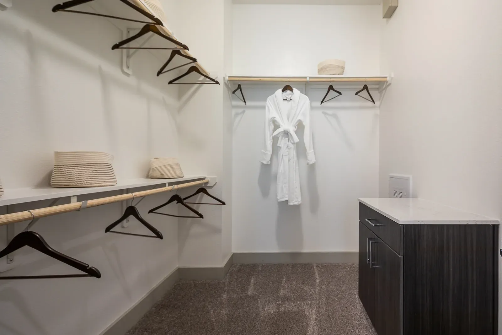 Walk-in closet with white shelving, wood hangers, and a white robe hanging.
