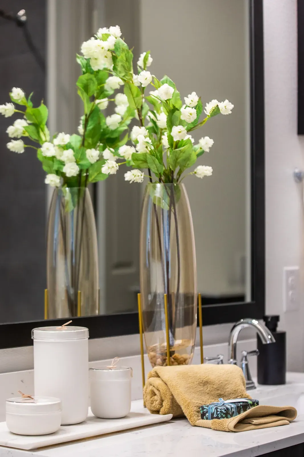 Close-up of a bathroom vanity with decorative flowers, toiletries, and a rolled towel.
