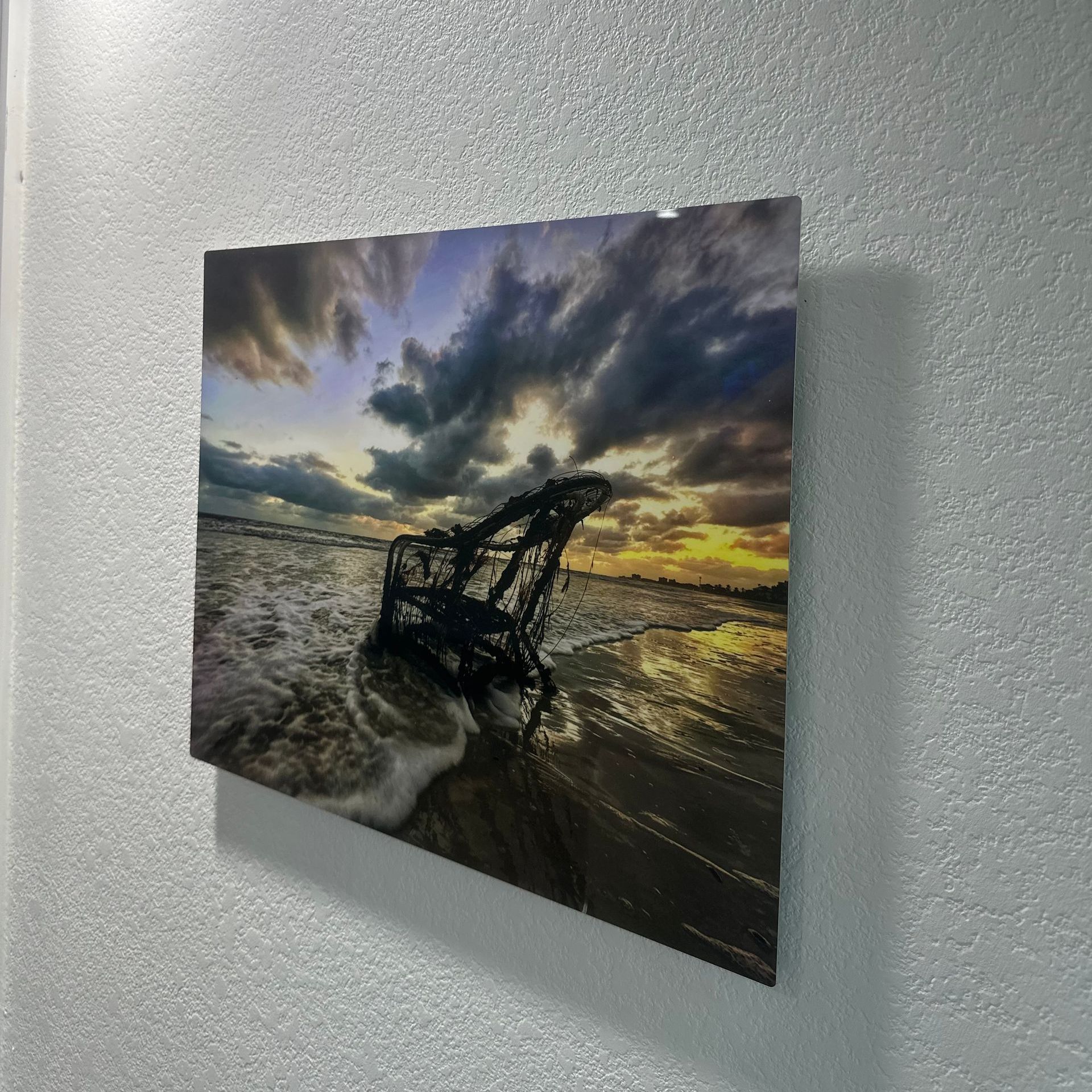 A painting of a chair on the beach is hanging on a white wall.