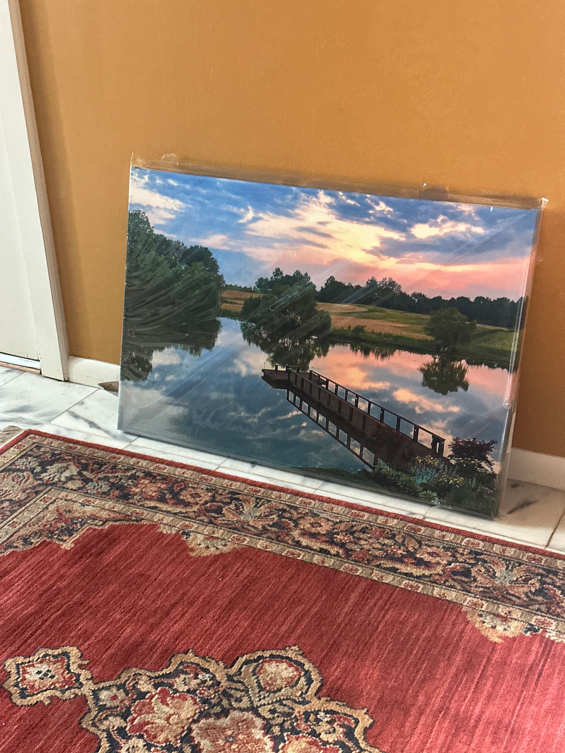 A painting of a bridge over a river is sitting on a rug.