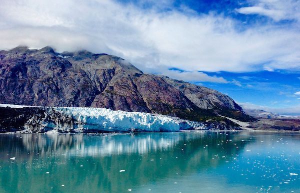 A large glacier is sitting in the middle of a lake surrounded by mountains.