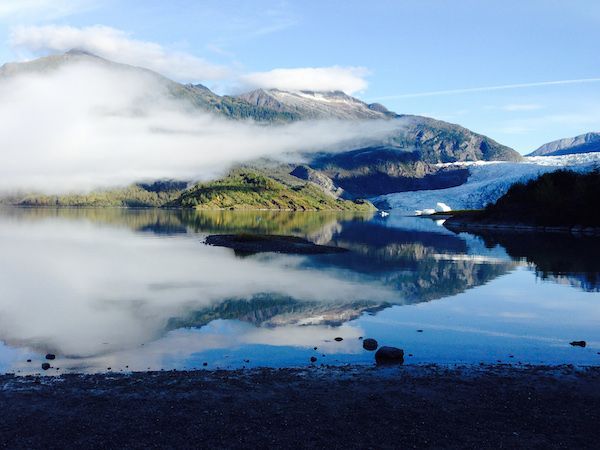 A lake with mountains in the background and clouds floating over it