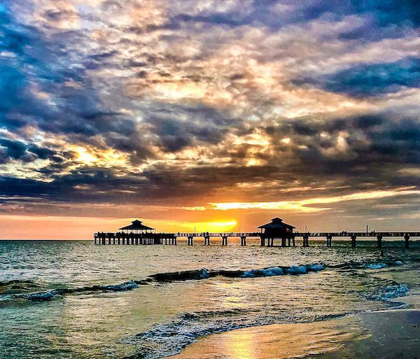 The sun is setting over the ocean with a pier in the foreground.