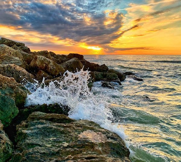A sunset over the ocean with waves crashing against the rocks