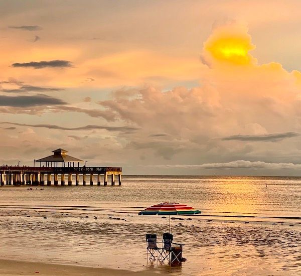A beach with chairs and an umbrella at sunset