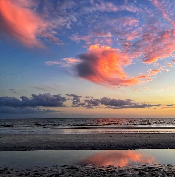 A beach at sunset with a reflection of the clouds in the water.