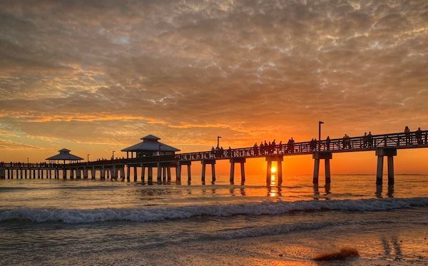 A pier overlooking the ocean at sunset with people walking on it