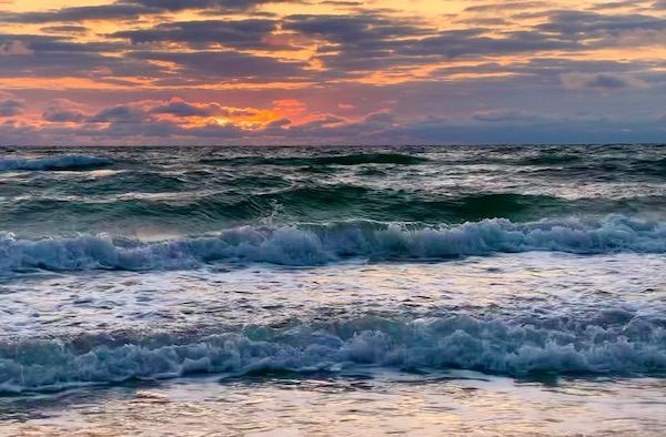 A sunset over the ocean with waves crashing on the beach.