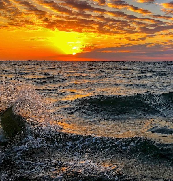 A sunset over the ocean with waves crashing on the shore
