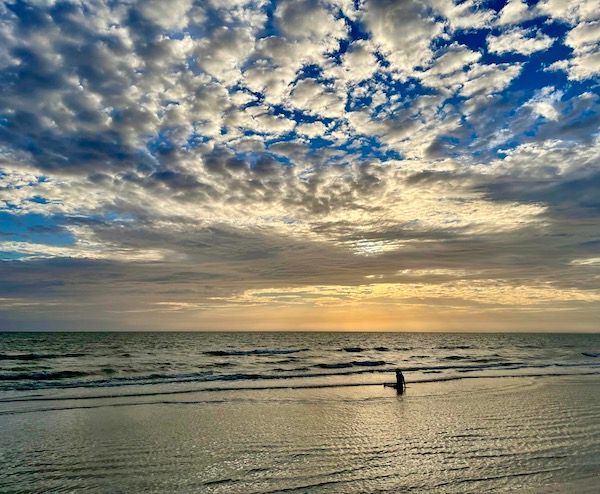 A person is walking on the beach at sunset.