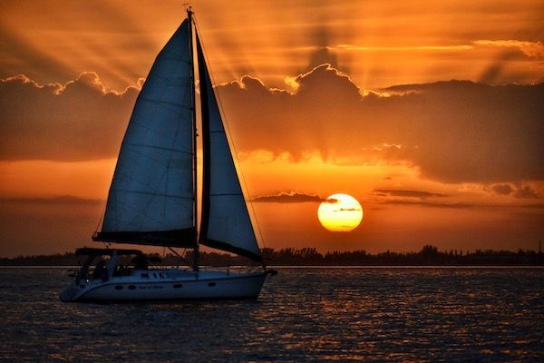 A sailboat is floating in the water at sunset