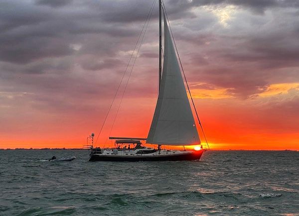 A sailboat is floating in the ocean at sunset