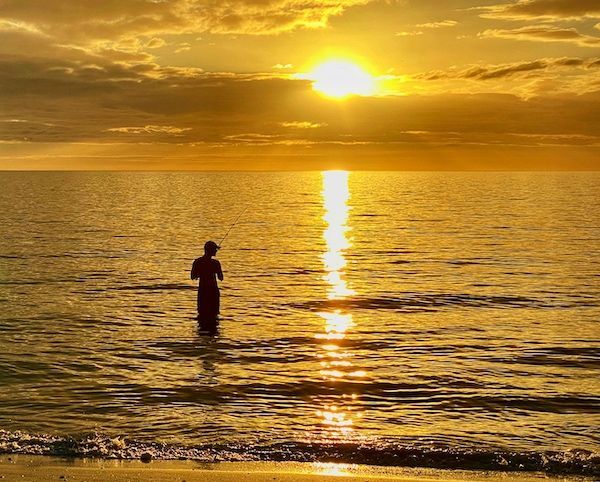 A person is standing in the ocean at sunset