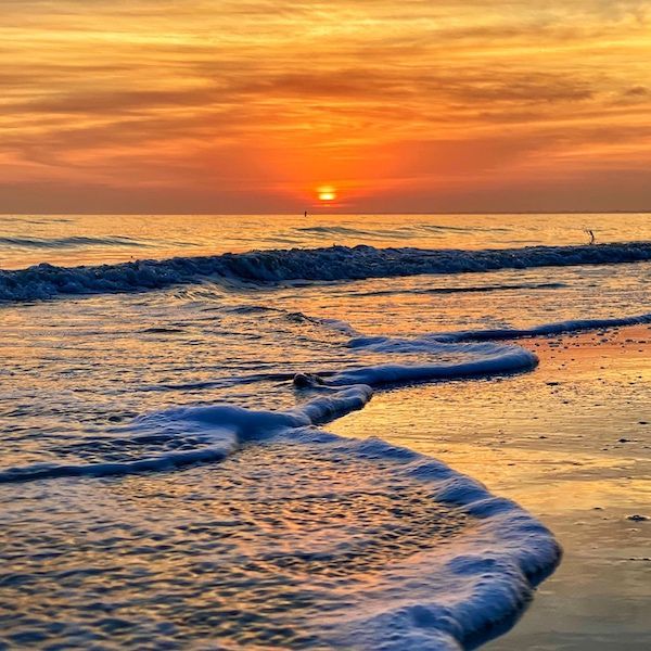 A sunset over the ocean with waves crashing on the beach