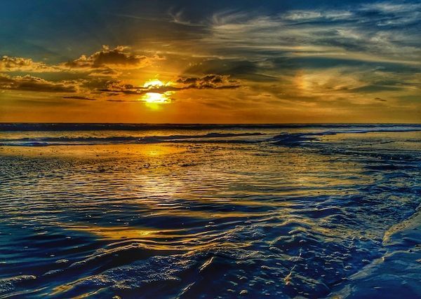 The sun is setting over the ocean and the waves are crashing on the beach.