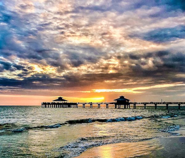 The sun is setting over the ocean with a pier in the foreground.