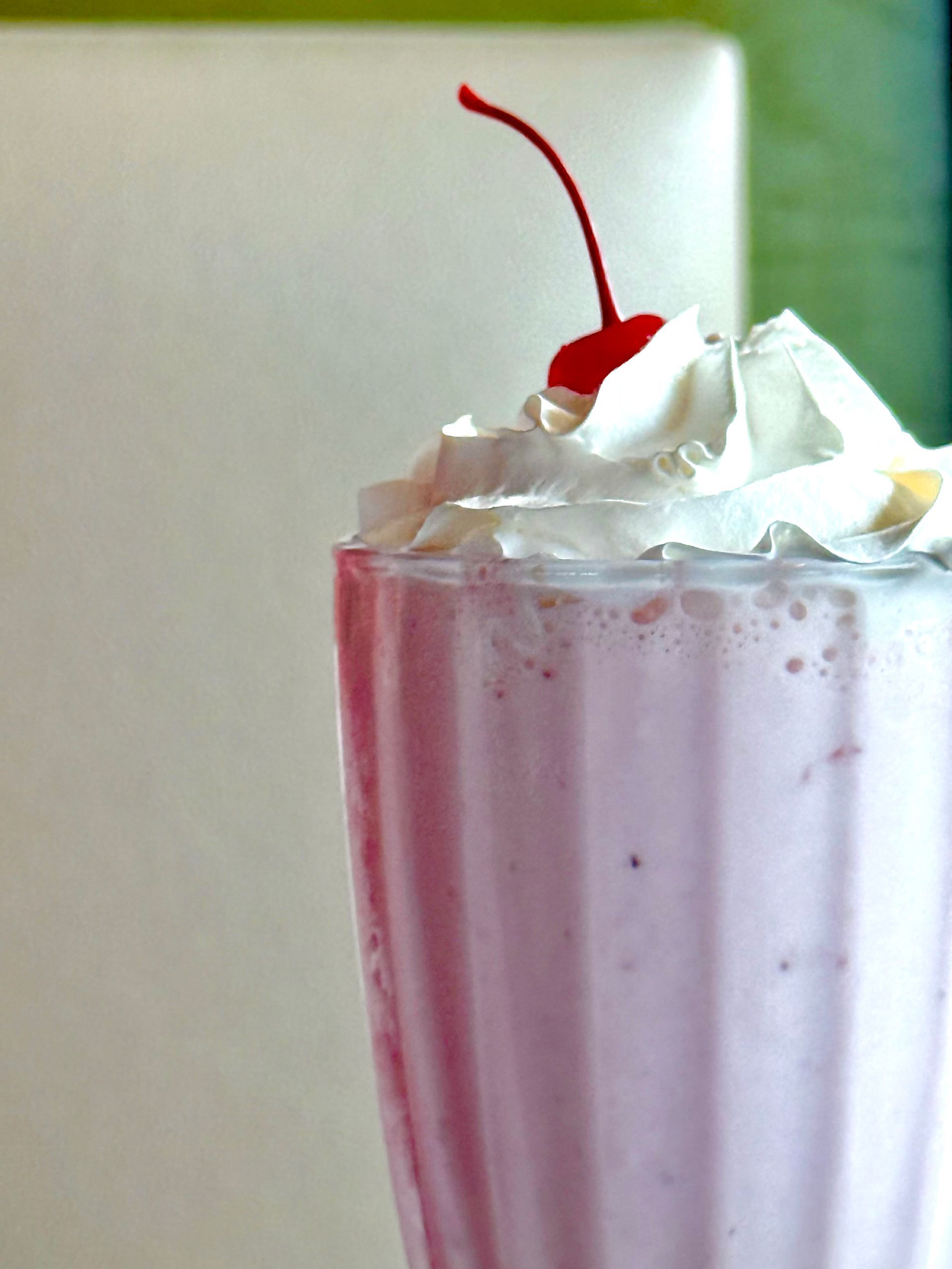 A pink milkshake with whipped cream and a cherry on top