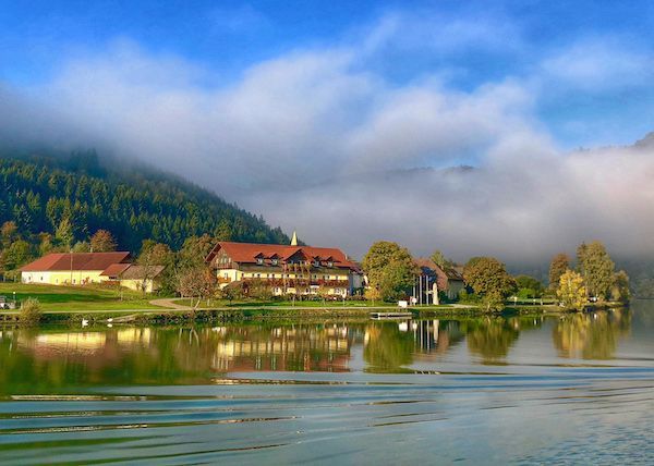 A lake with a house on the shore and mountains in the background.