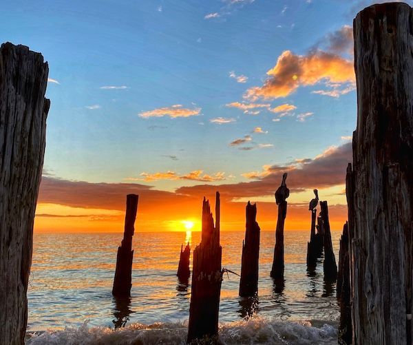 A sunset over a body of water with wooden posts in the foreground