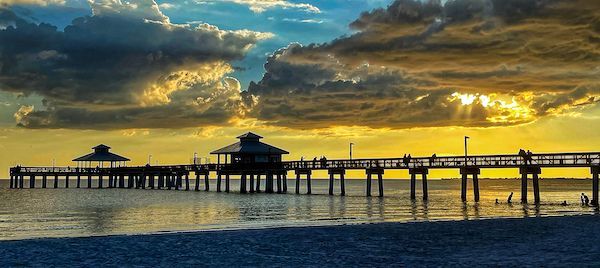 There is a pier in the middle of the ocean at sunset.