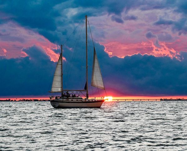 A sailboat is floating on top of a body of water at sunset.
