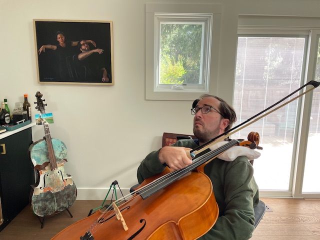 A man is playing a cello in a living room.