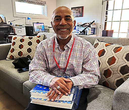Marchell smiling, sitting on a couch, holding notebooks