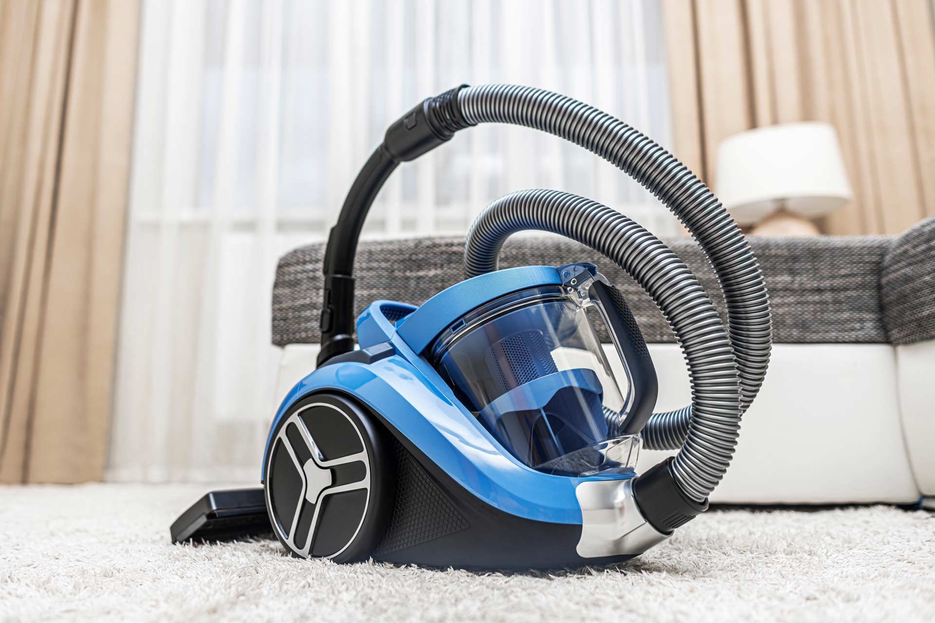 Blue and black vacuum cleaner on white carpet in a living room.
