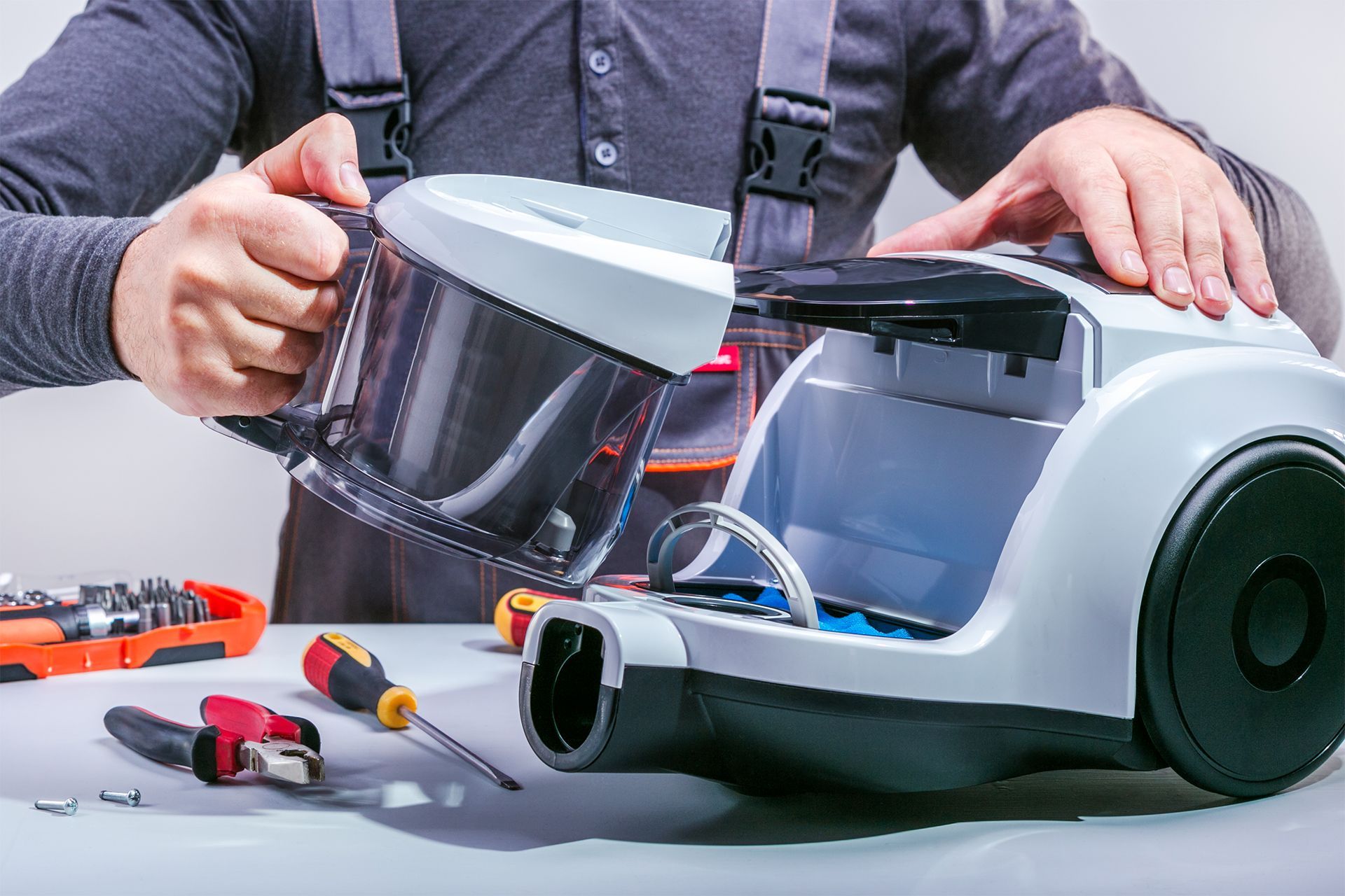 Person repairing vacuum cleaner with tools on a table.