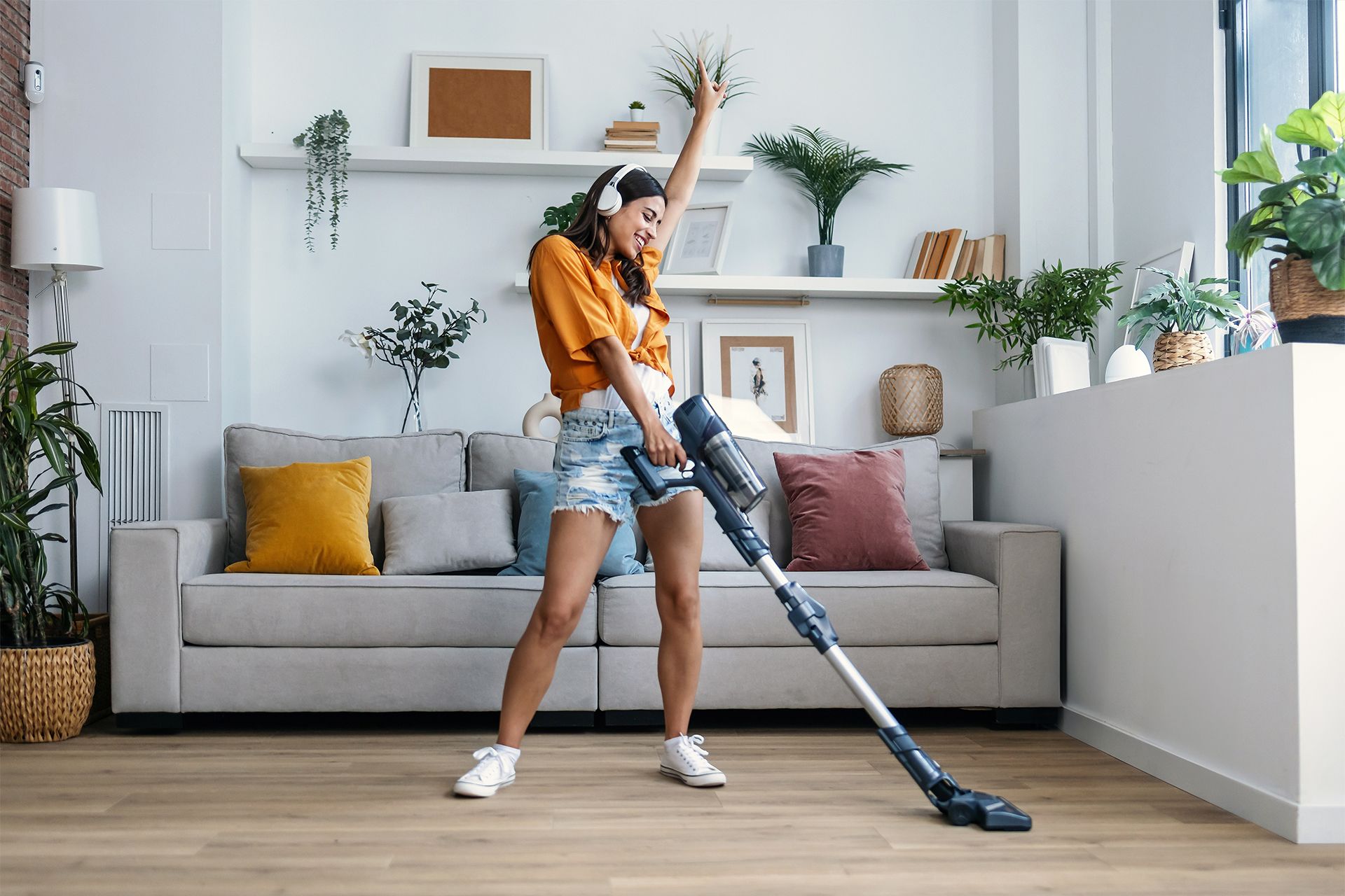 Woman dances while vacuuming her living room, wearing headphones and shorts.