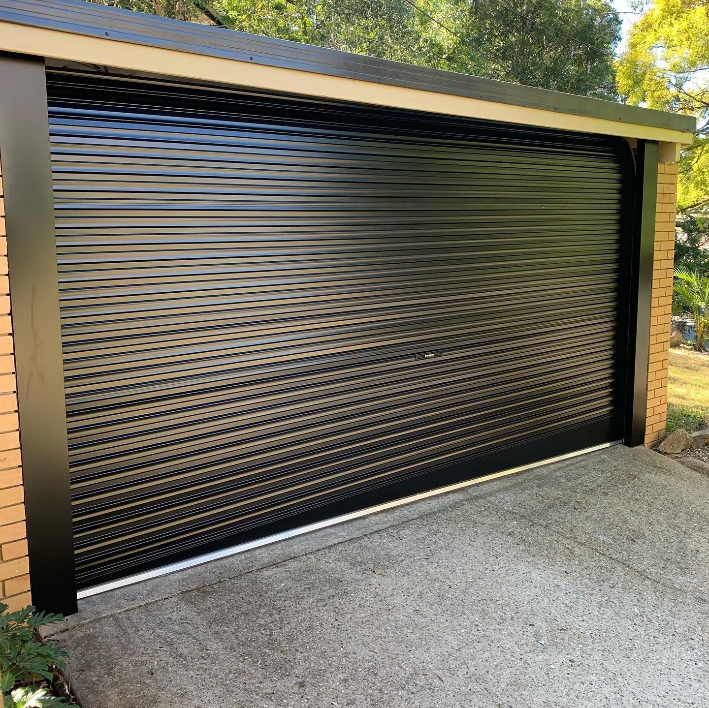 A black garage door is sitting next to a brick building.