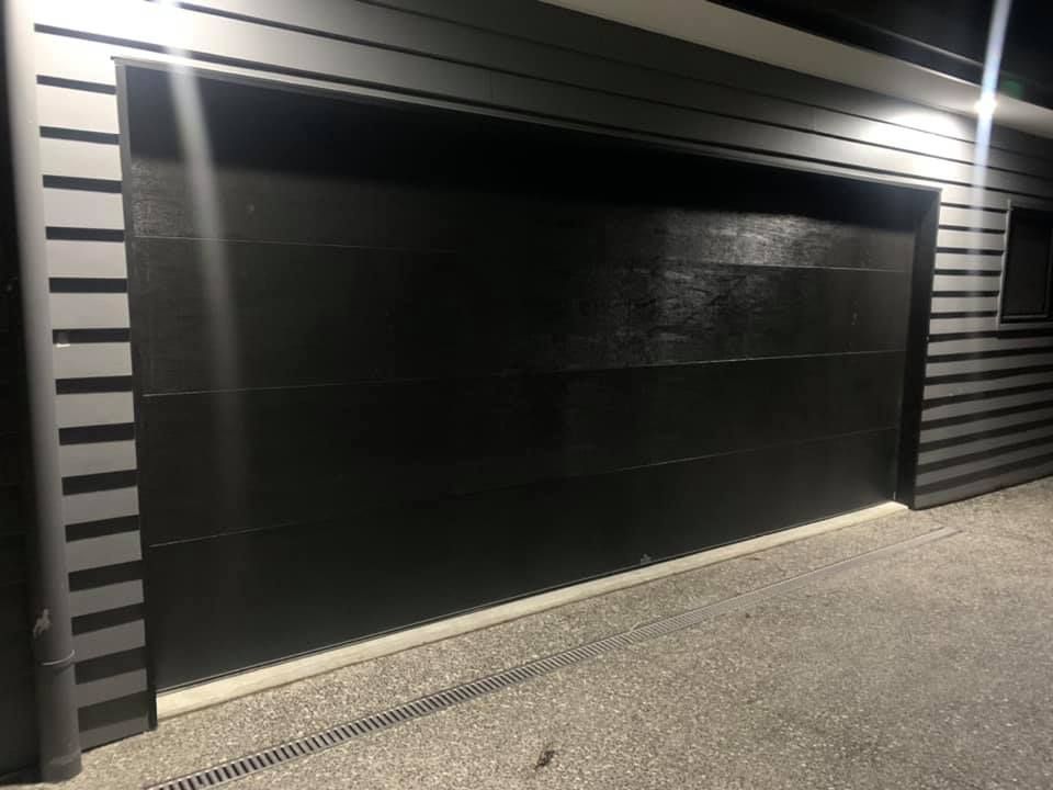 A black garage door is lit up at night.