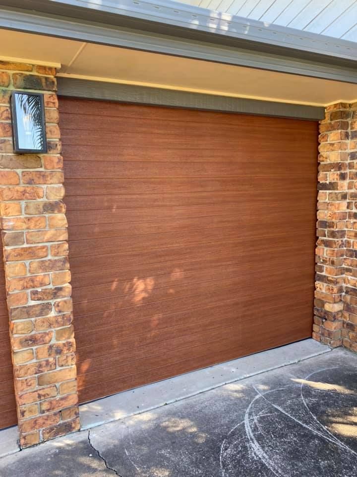 A brown garage door is sitting next to a brick wall.