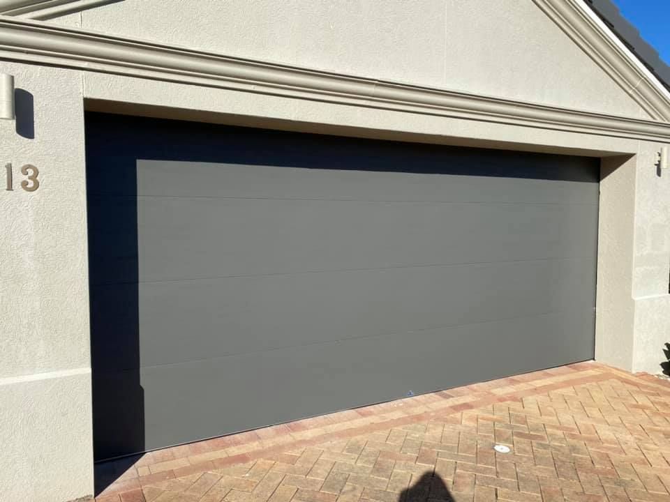 A gray garage door is on the side of a house.