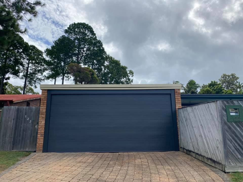 A blue garage door is sitting next to a brick fence.