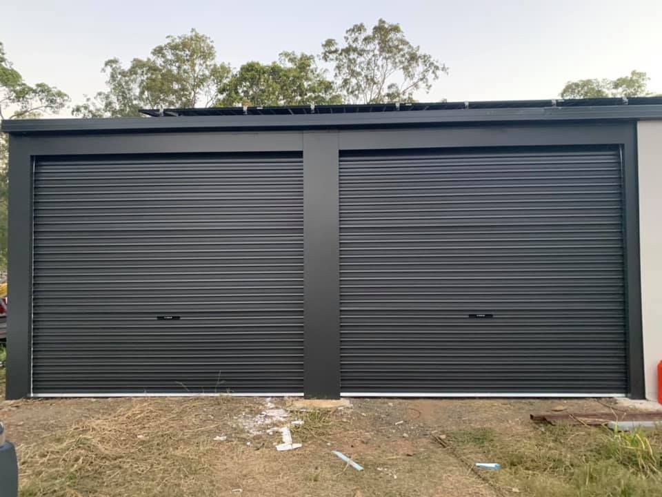 A garage with two black garage doors is sitting on top of a grassy hill.