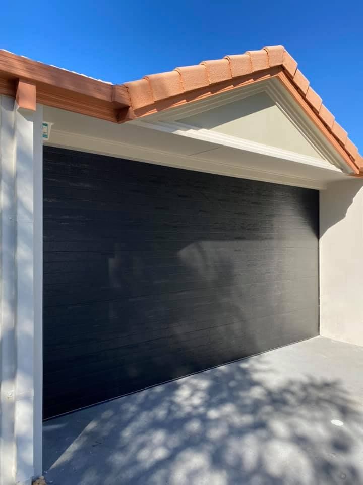 A black garage door with a tiled roof and a blue sky in the background.