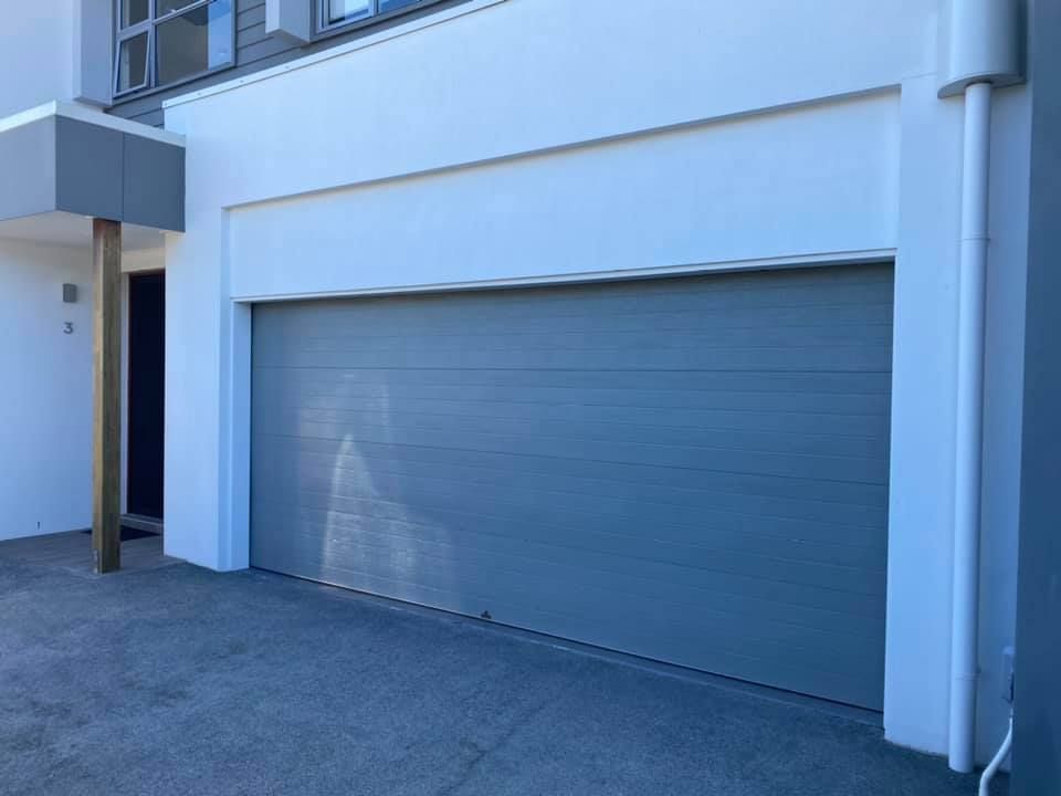 A gray garage door is on the side of a white building.