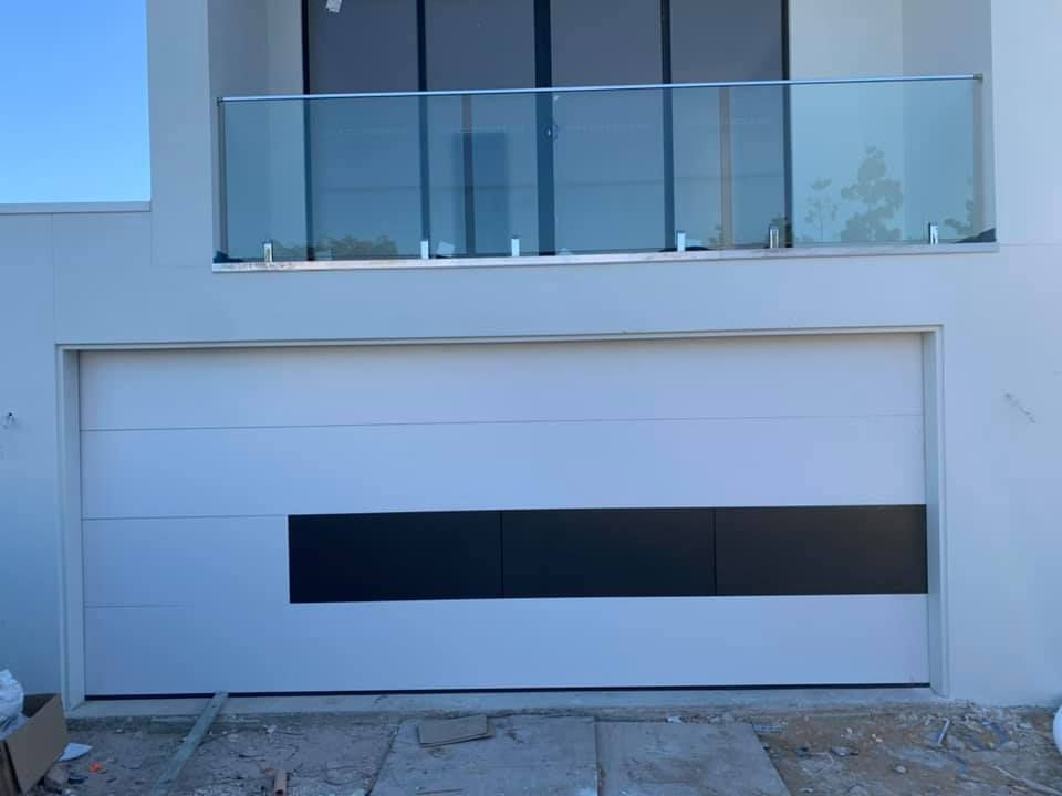 A white garage door with a black stripe and a balcony.