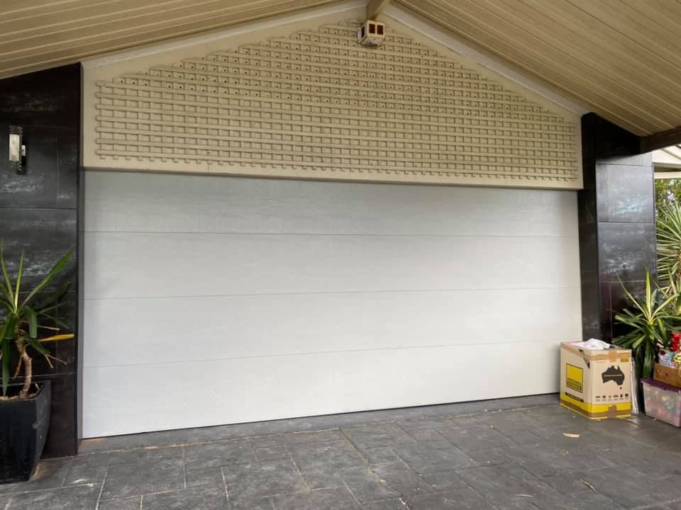 A white garage door is sitting in front of a house.