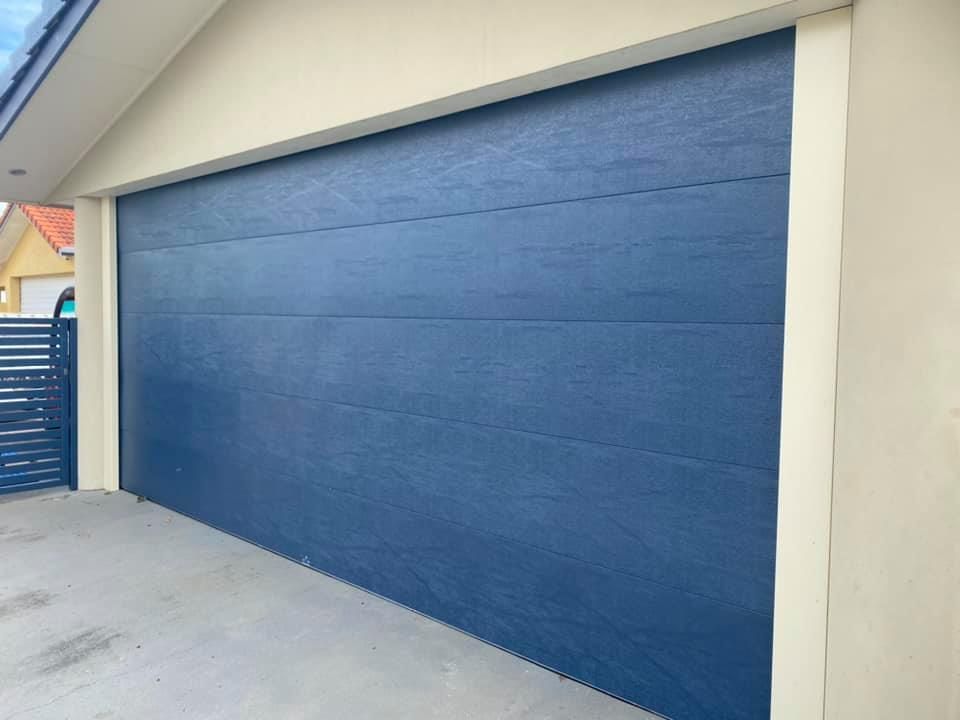 A blue garage door is sitting on the side of a house.