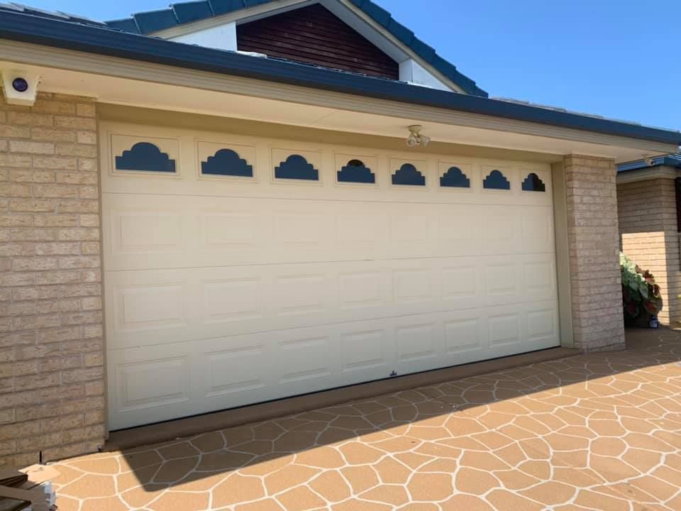 A white garage door with black clouds on it is in front of a brick house.