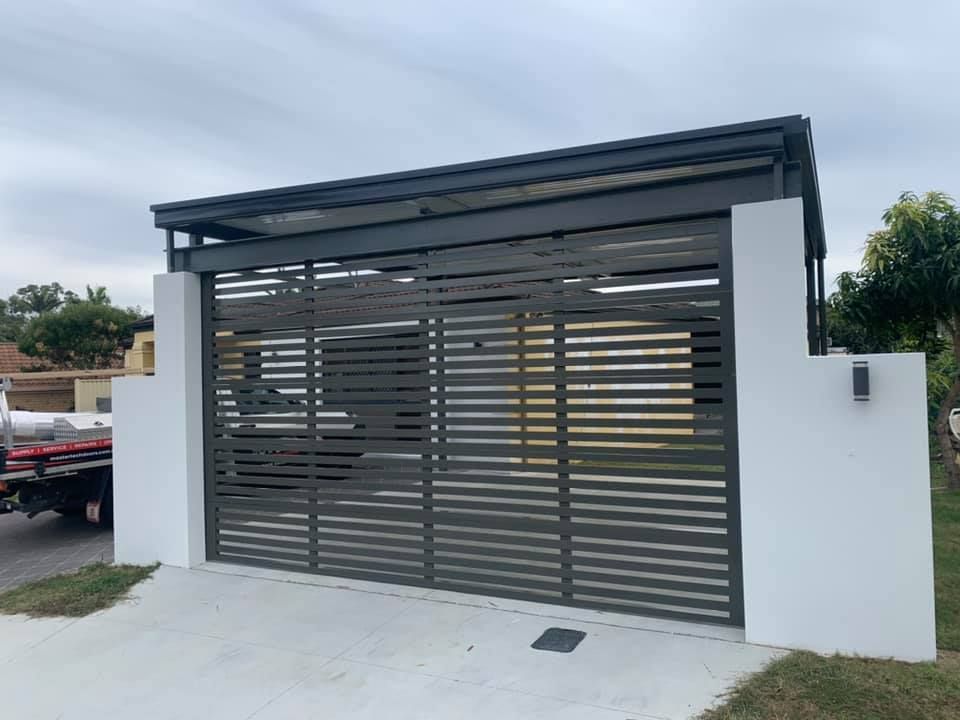 A white wall with a black gate and a truck parked in front of it.