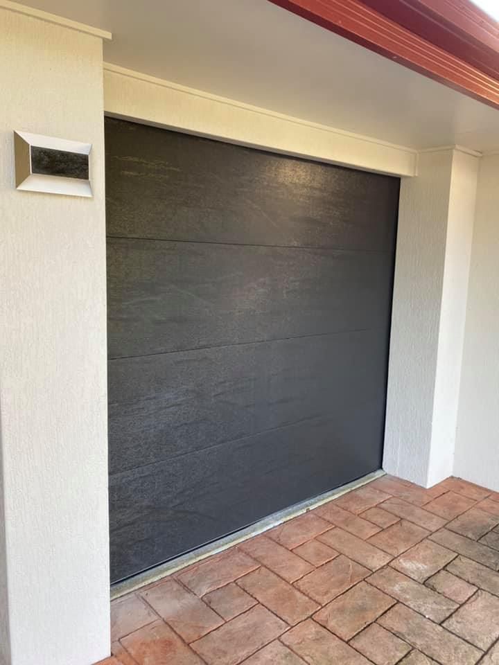 A black garage door is sitting on a tiled floor next to a white wall.