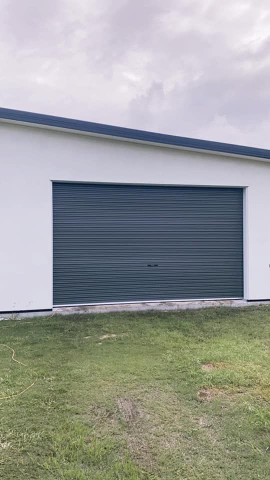 A white garage with a blue garage door is sitting in the middle of a grassy field.