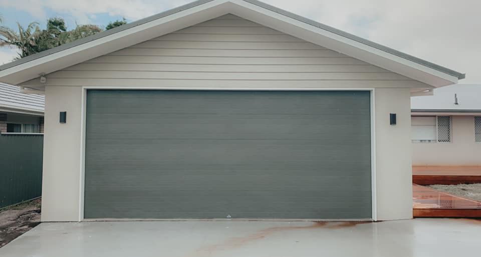 A garage with a gray garage door and a white house in the background.