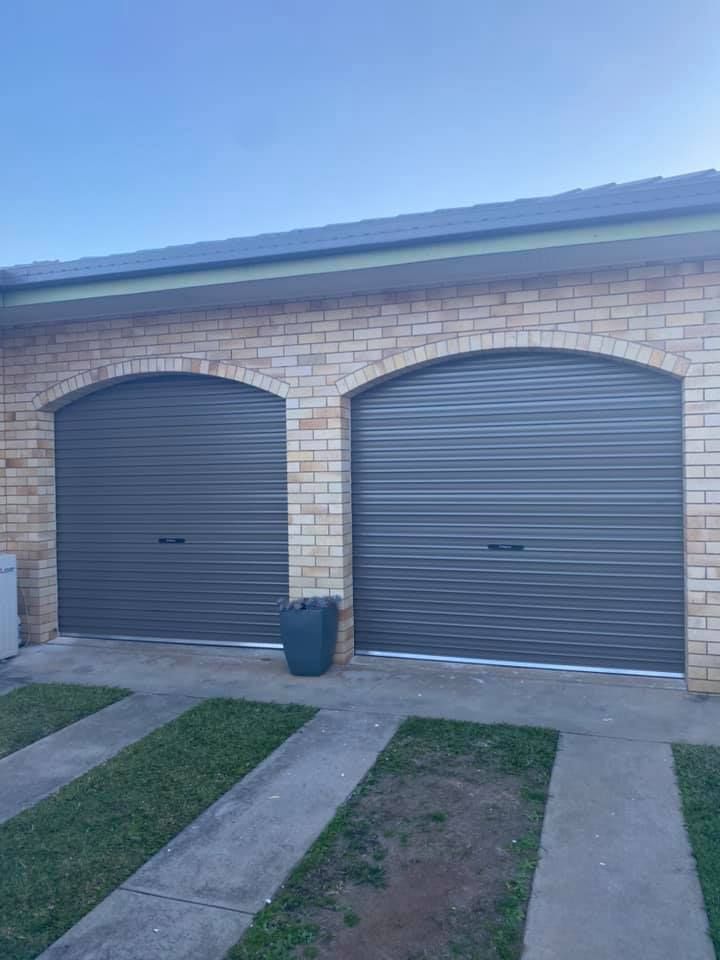 There are two garage doors on the side of a brick house.