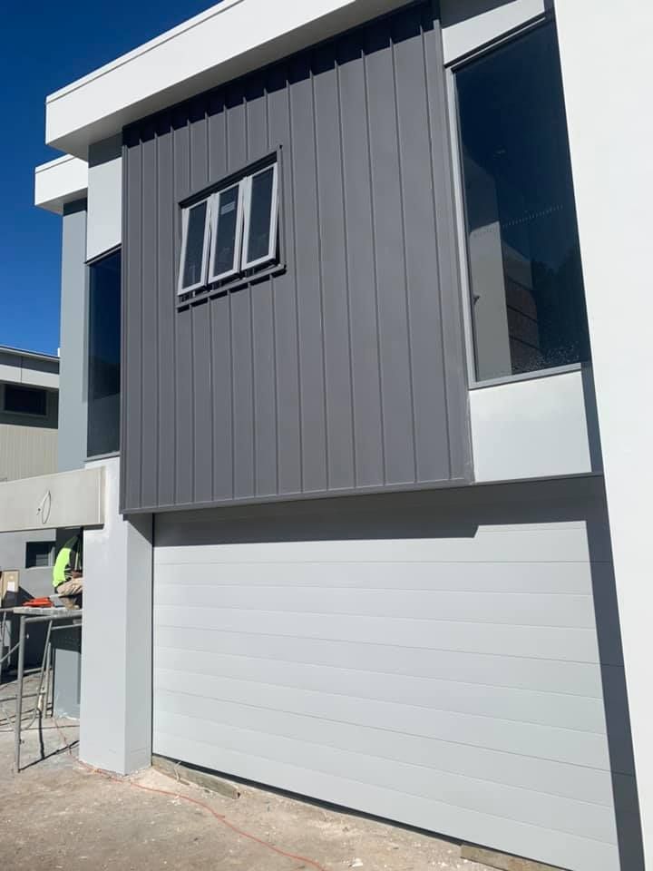 A white house with a gray siding and a white garage door.