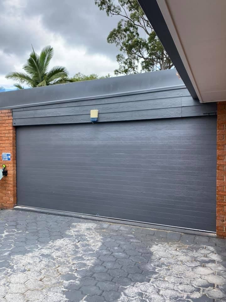 A large gray garage door is sitting in front of a brick building.