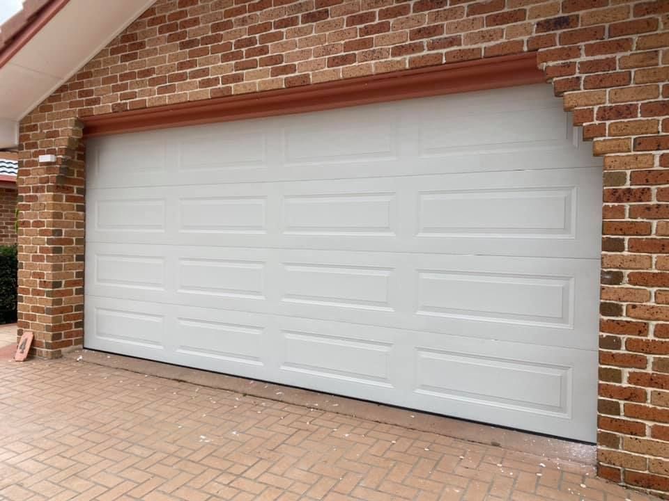 A white garage door is sitting in front of a brick building.